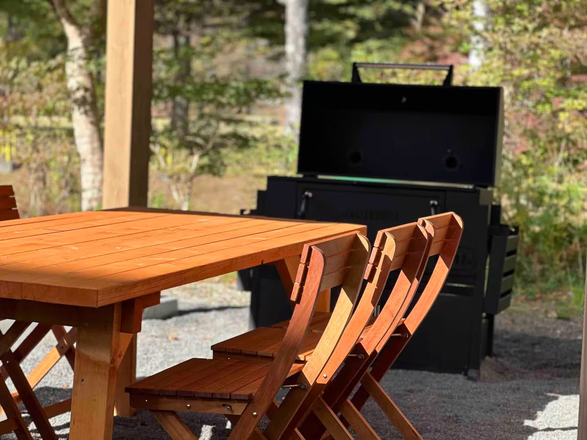 木のテーブルと椅子、その奥に蓋付きの大きなBBQグリル